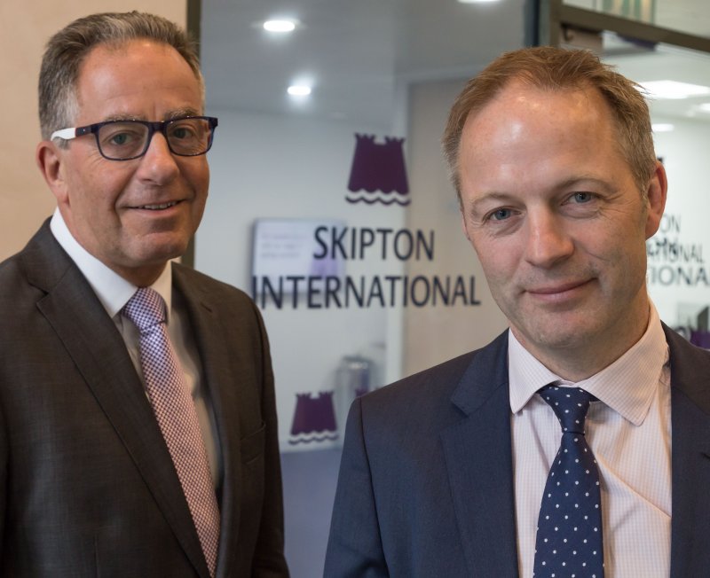 Two men smiling Infront of Skipton logo