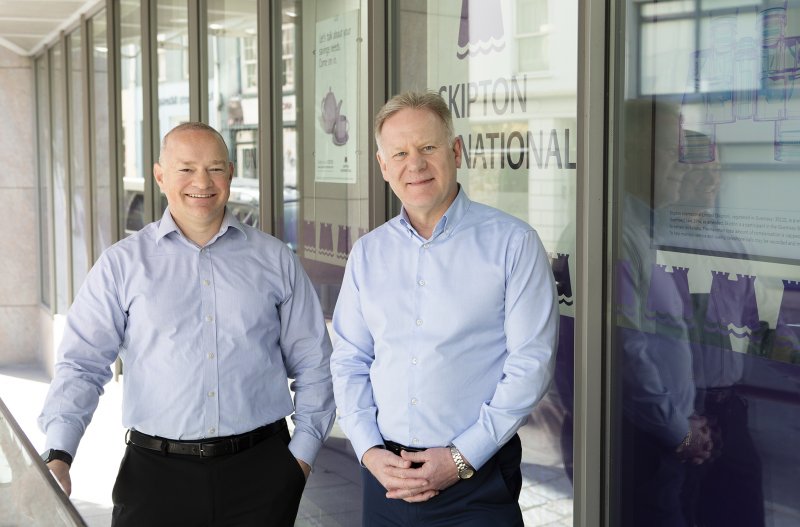 Two men smiling Infront of Skipton logo